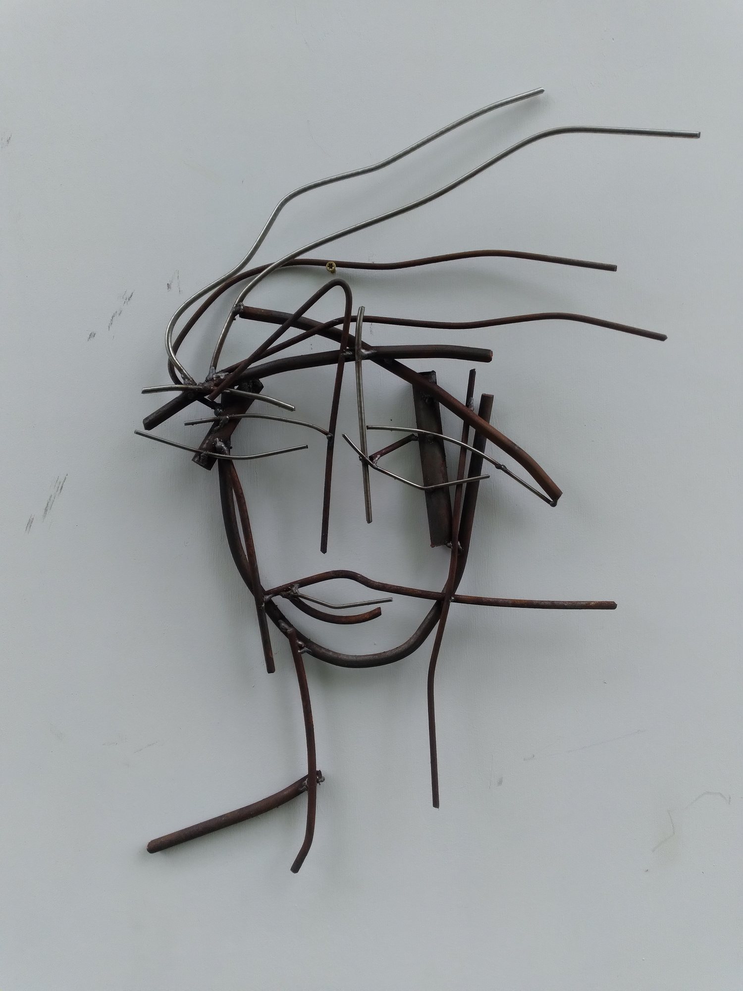 Drawing lines. A face in welded steel rod on a pale wall.
